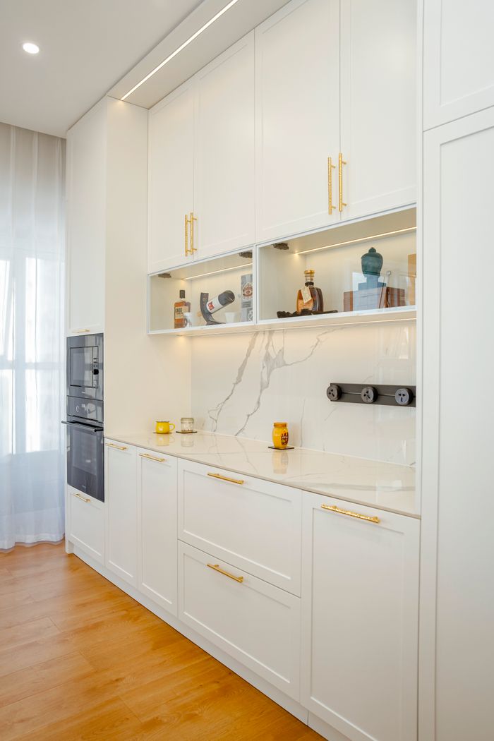 About Bright modern kitchen with sleek white cabinets, marble details, and wooden flooring.